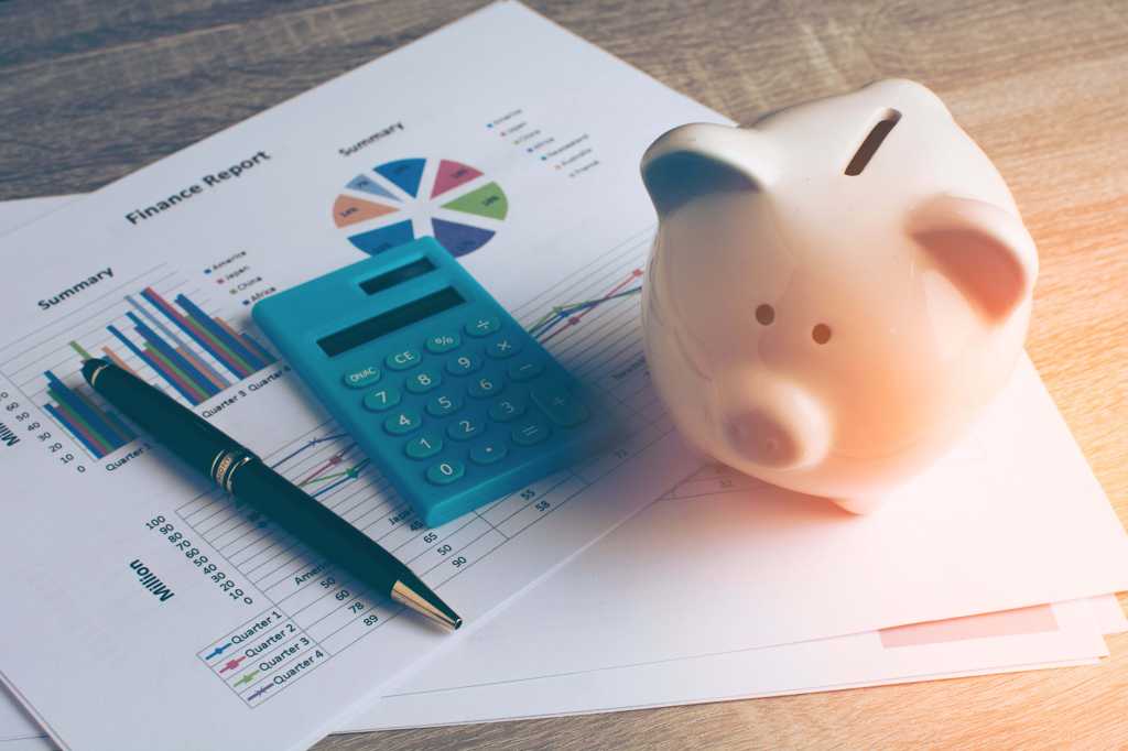 A calculator and piggy bank sit on printouts of financial graphs.