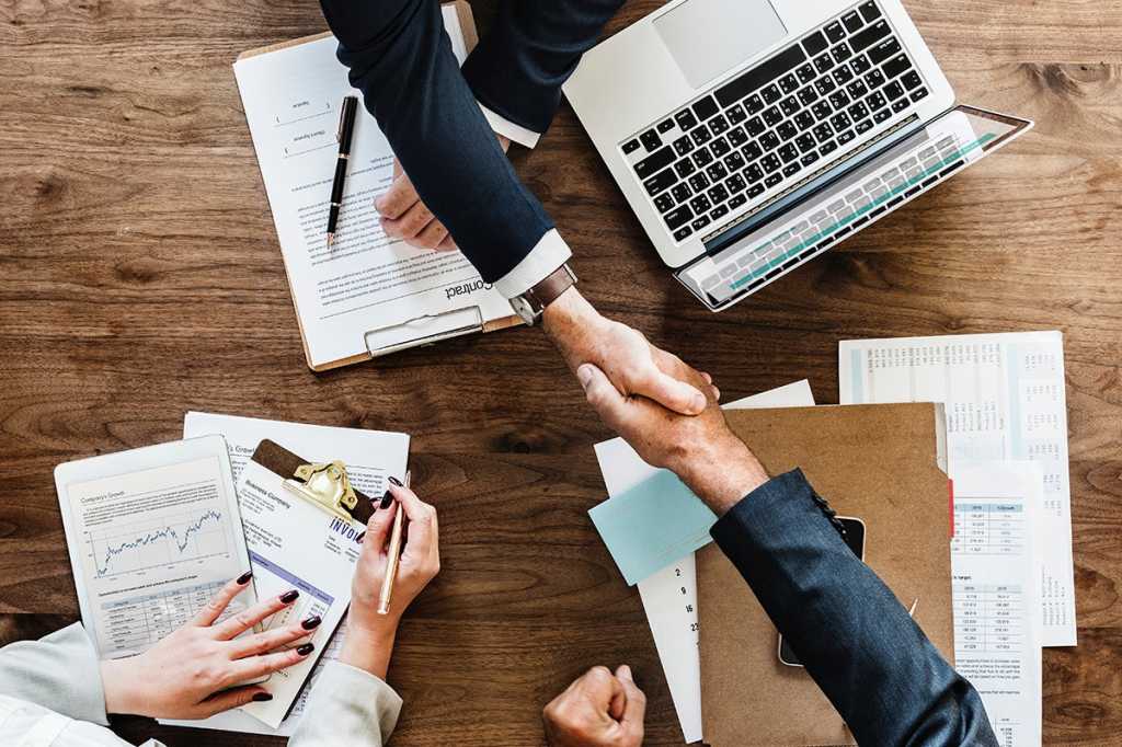 Two people shake hands over a laptop.