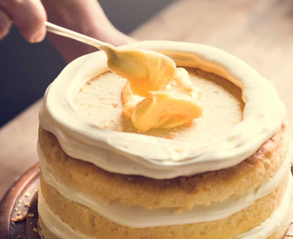 shutterstock 1104796700 layer cake with white and yellow frosting on a wooden table