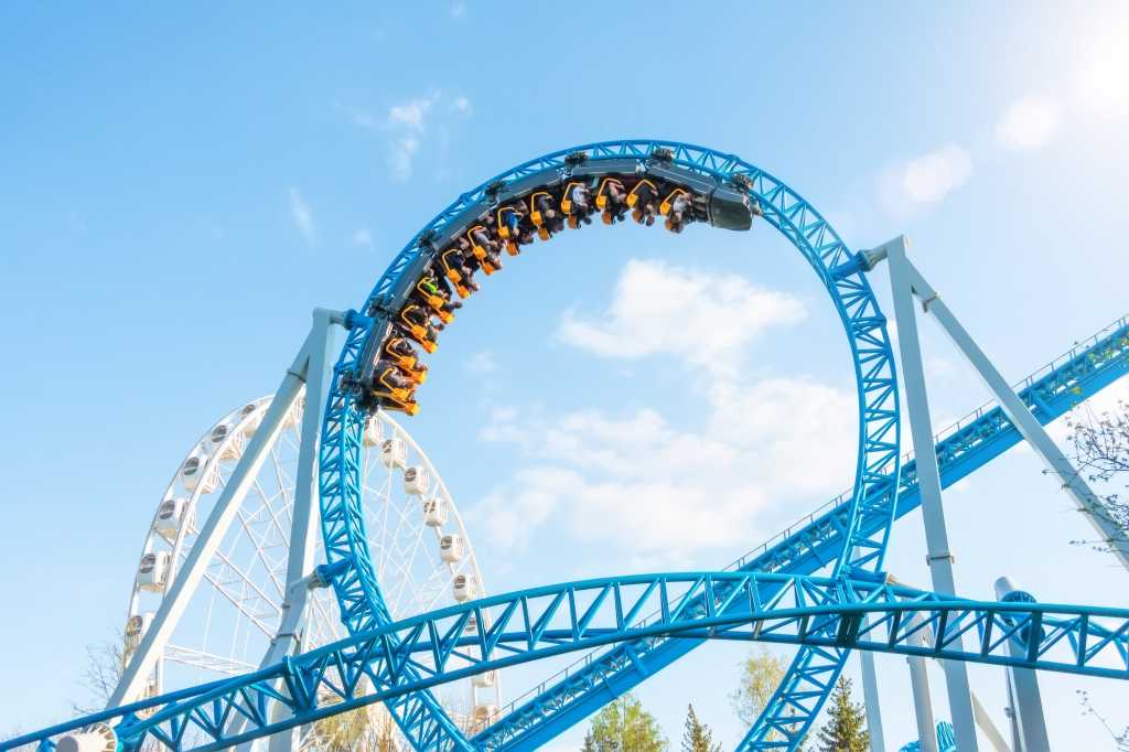 upside down roller coaster in a loop against a cloud and blue sky amusement park