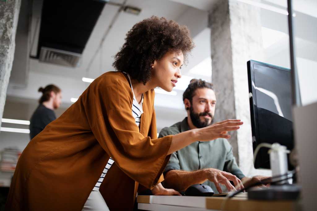 Two developers / programmers collaborate as they review information on a display in their workspace.